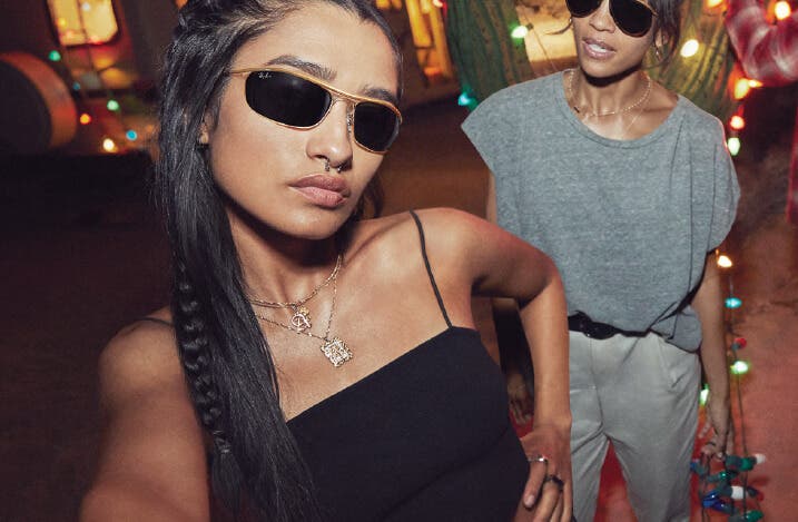 young woman wearing ray ban sunglasses rb3119 olympian in gold with g-15 lenses and another woman wearing ray ban rb3025 aviator in gold with g-15 lenses